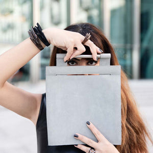 Black cuff bracelet presented by model hiding behind a bag.