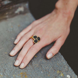 Geometric ring gold black on finger in front of concrete wall.