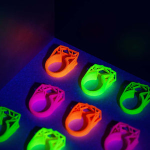 A neon orange ring with other neon jewelry under UV light.