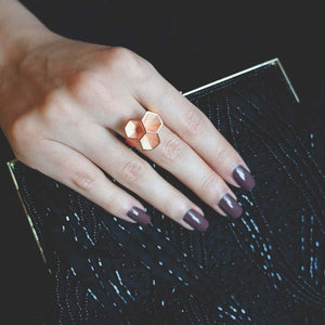 Rose gold honeycomb ring on finger in front of a nice bag.