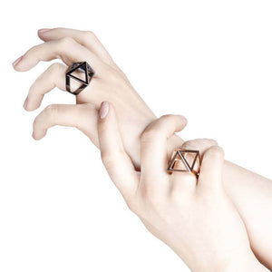 Rosegold pyramid ring and black rhodium ring on hands reaching up.